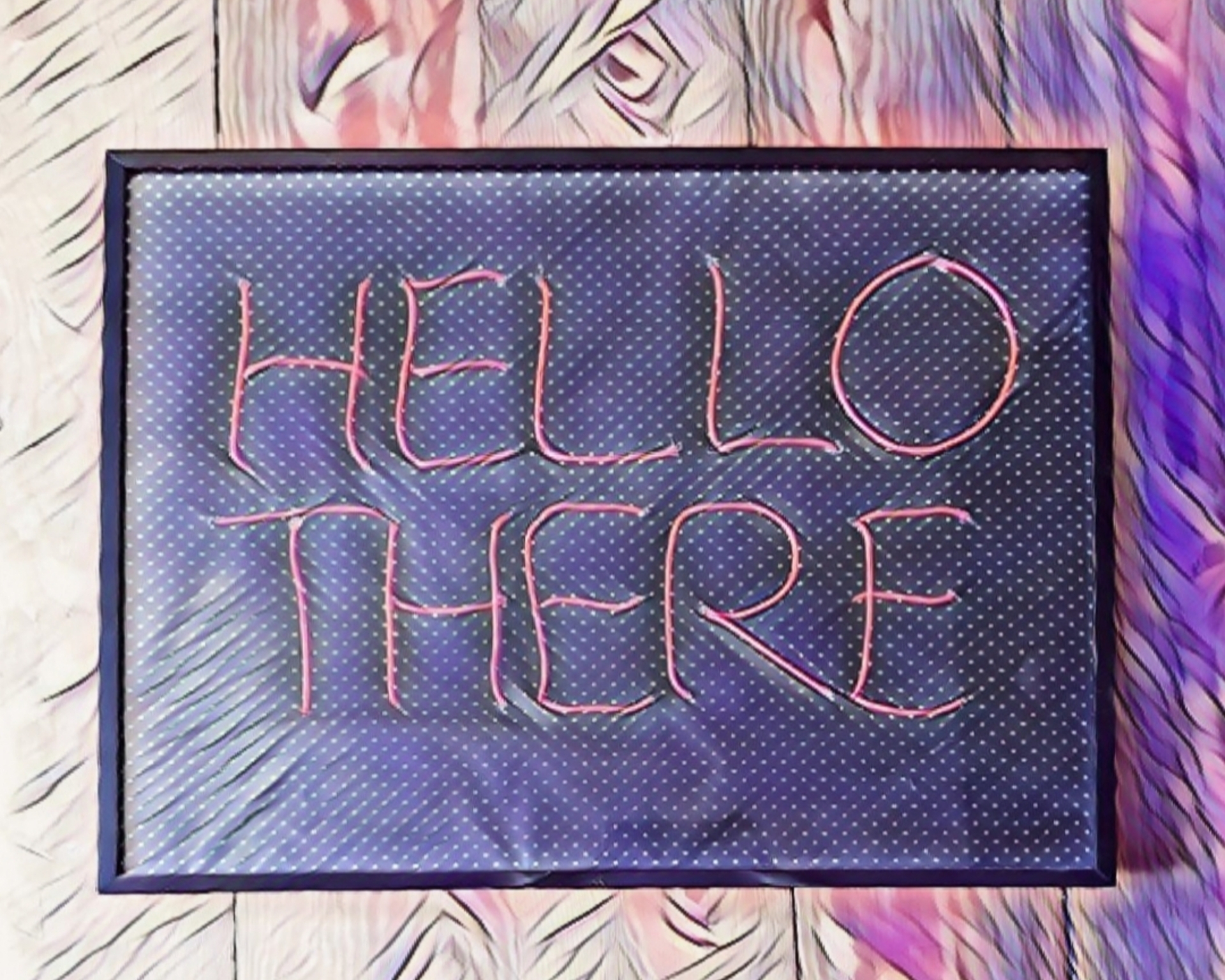 Ein mit Filtern bearbeitetes Foto von einem Schild mit dem Schriftzug "HELLO THERE" in rosa Buchstaben auf schwarzem Hintergrund mit kleinen weißen Punkten in einem schwarzen Rahmen auf einem Holzhintergrund. Der Filter gibt dem ganzen einen illustrativen Anstrich und lila und pinke Schattierungen.
