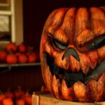 Ein Kürbis trägt eine Jack O'Lantern Fratze, die von außen geschnitzt und dann schwarz gemalt wurde. Auch wurden die Furchen des Kürbis dunkel gefärbt. Das verstärkt die düstere, knorrige Wirkung.